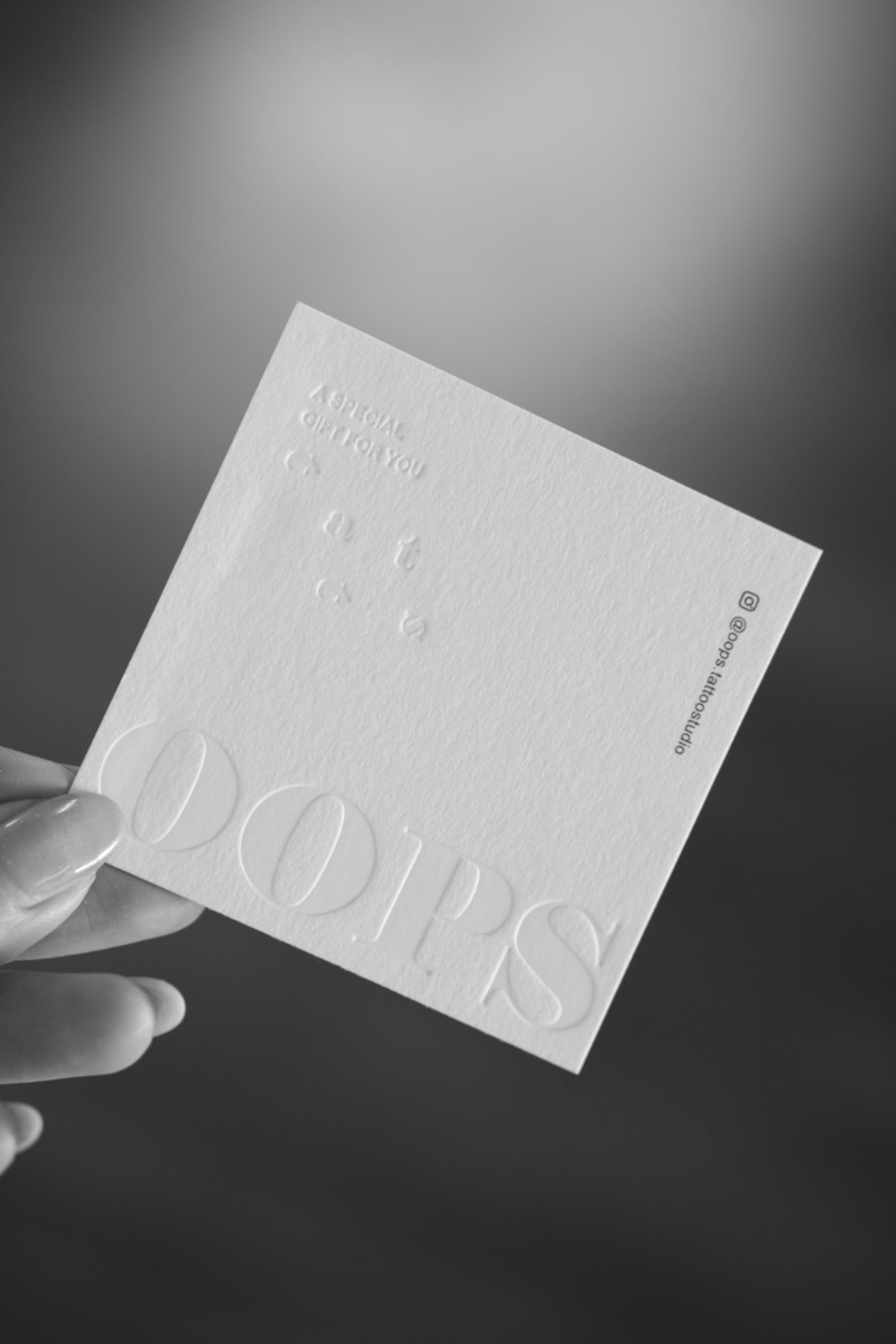 Embossed Oops Tattoo Studio card, held in hand